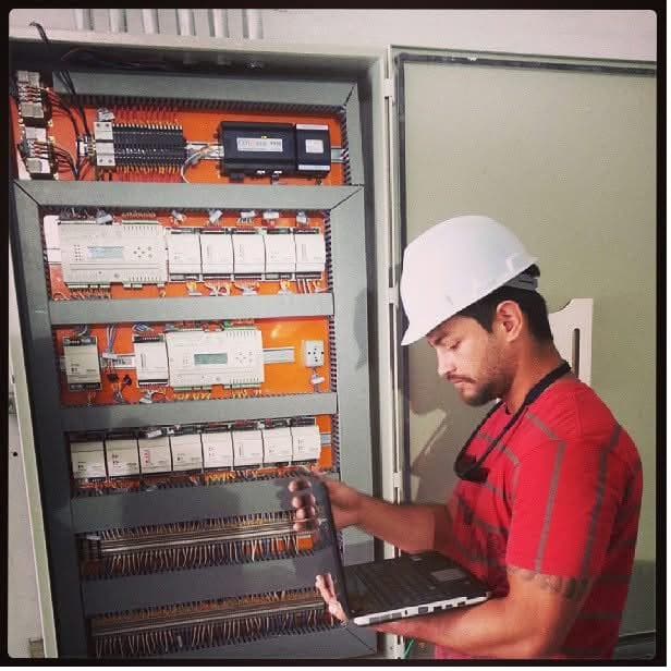 Thenperson, de capacete, mexendo em um painel elétrico durante trabalho como técnico de automação.